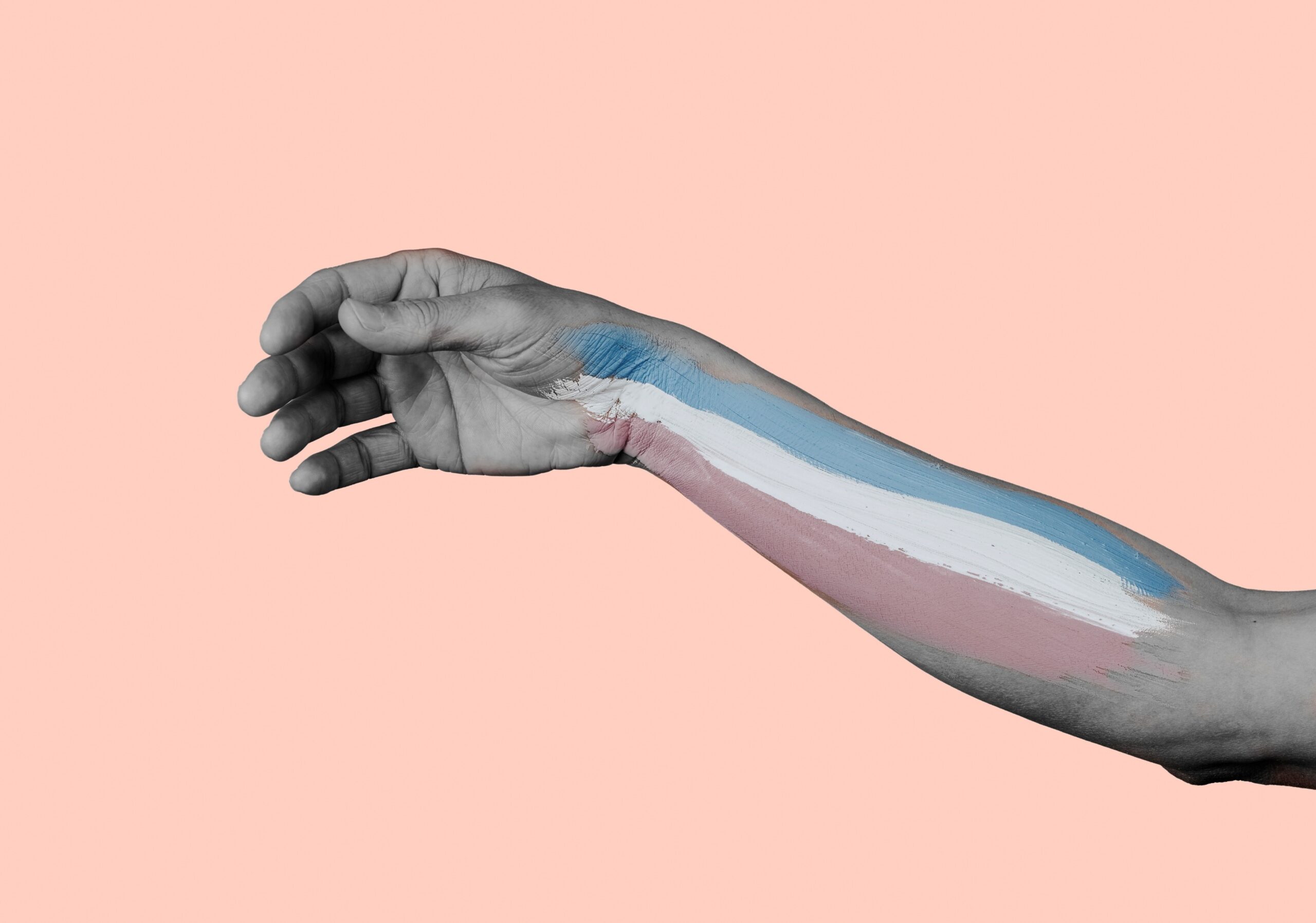 A greyscale arm on a baby pink background. The arm has the trans flag painted on it from wrist to elbow.